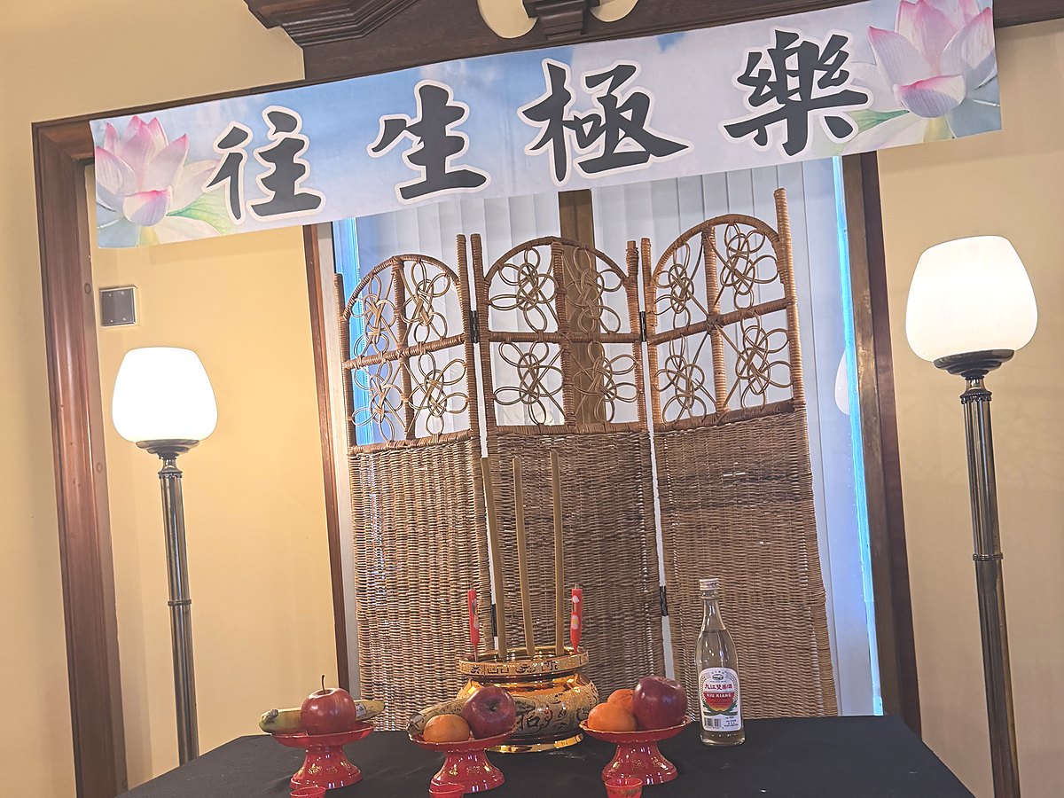 An altar prepared for a Buddhist service: a 往生極樂 banner, incense, candles, and fruit offerings